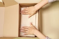 Close-up of hands packing a cardboard box with care using parchment paper.
